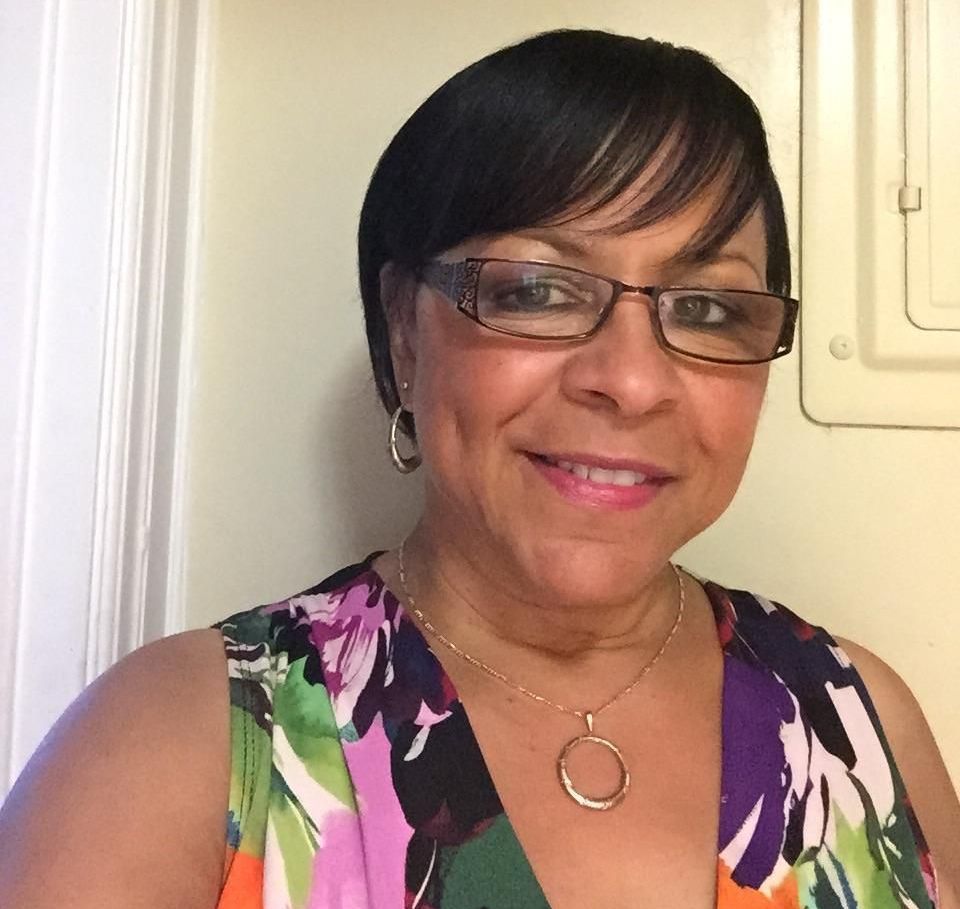 Smiling woman in glasses wearing a floral top and necklace indoors