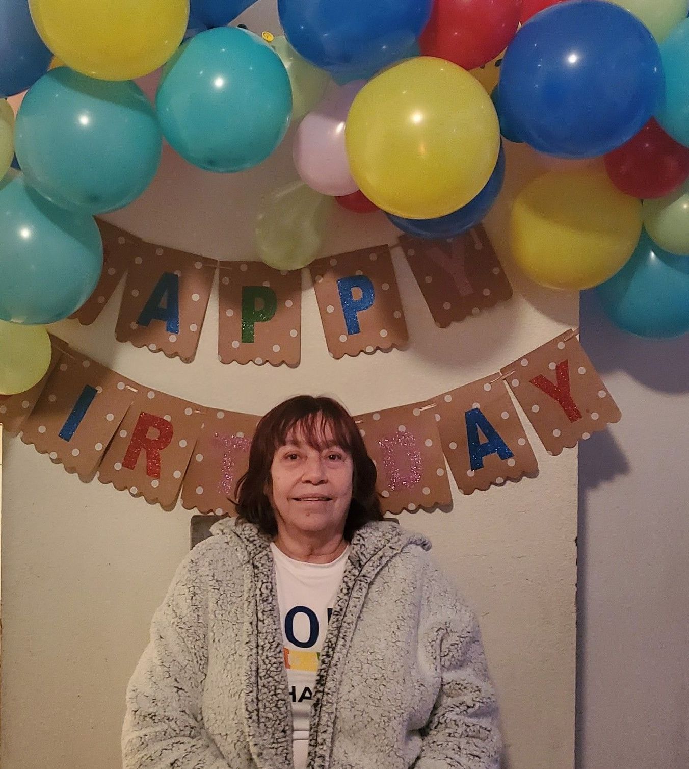 Woman standing under colorful balloons and a “Happy Birthday” banner at a party