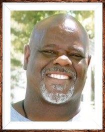 Smiling man with a bald head and gray goatee in a white-framed portrait outdoors