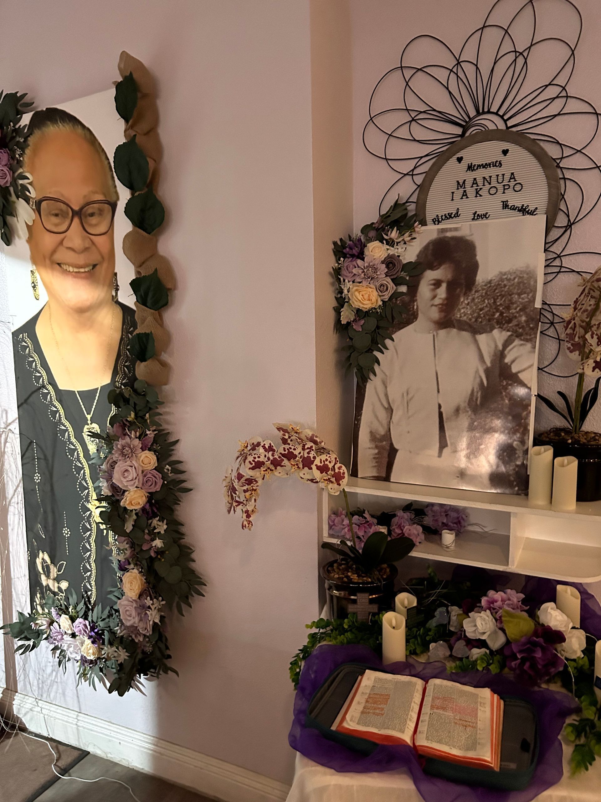 Memorial altar with framed portraits, flowers, candles, and an open guest book on a purple cloth.