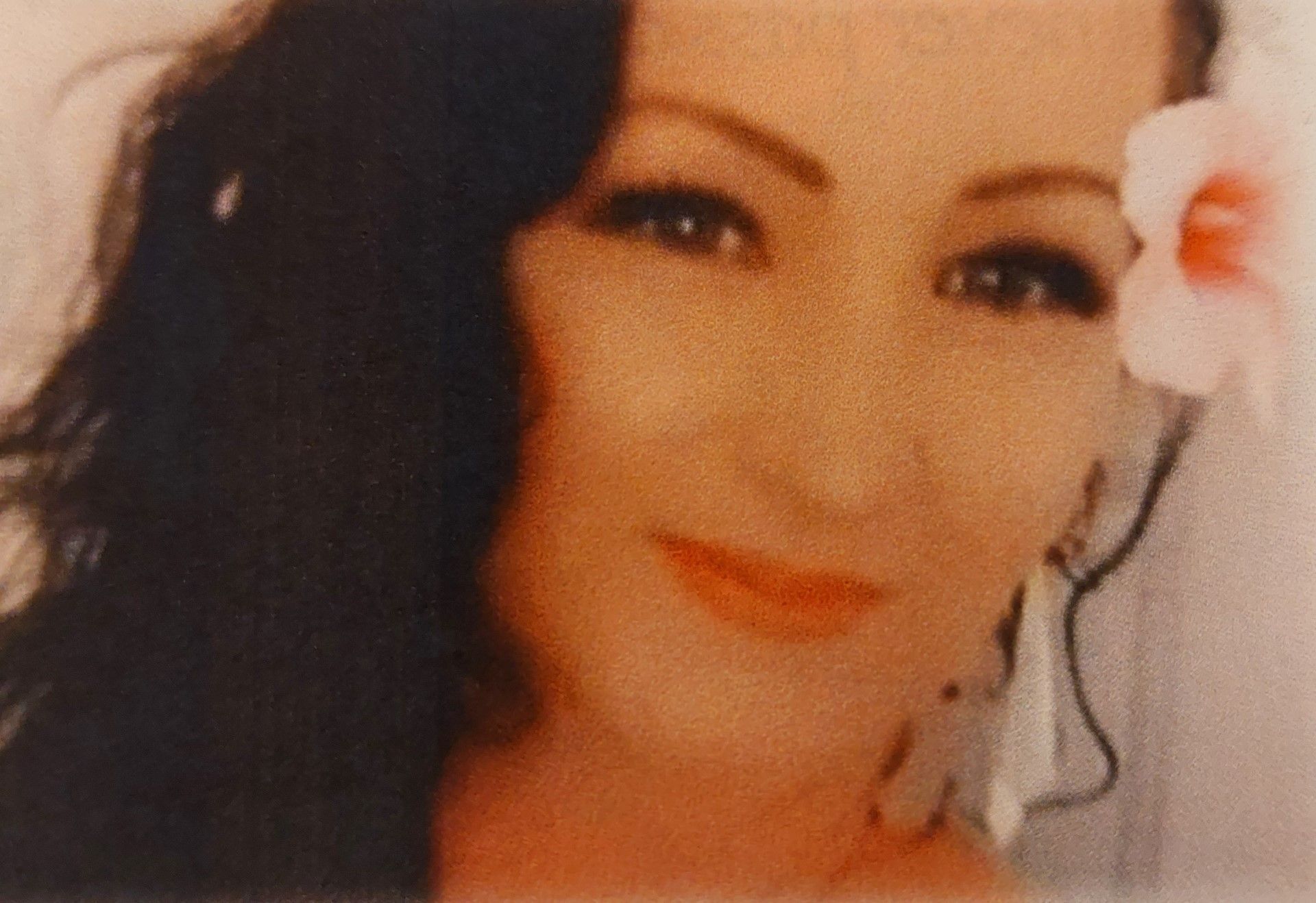 Close-up portrait of a smiling person with dark hair and a white flower by the ear