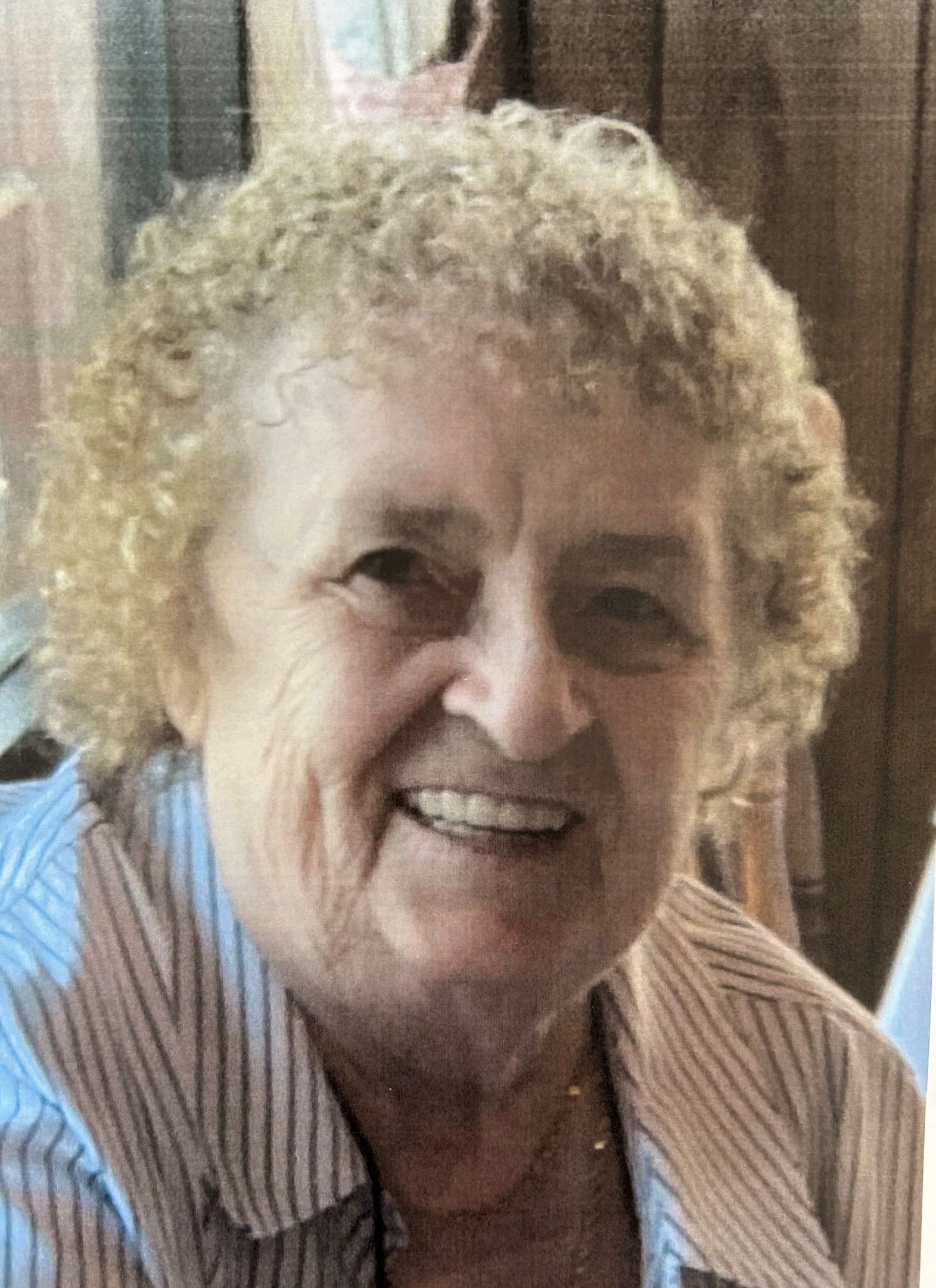 Smiling person with curly blond hair wearing a striped shirt indoors