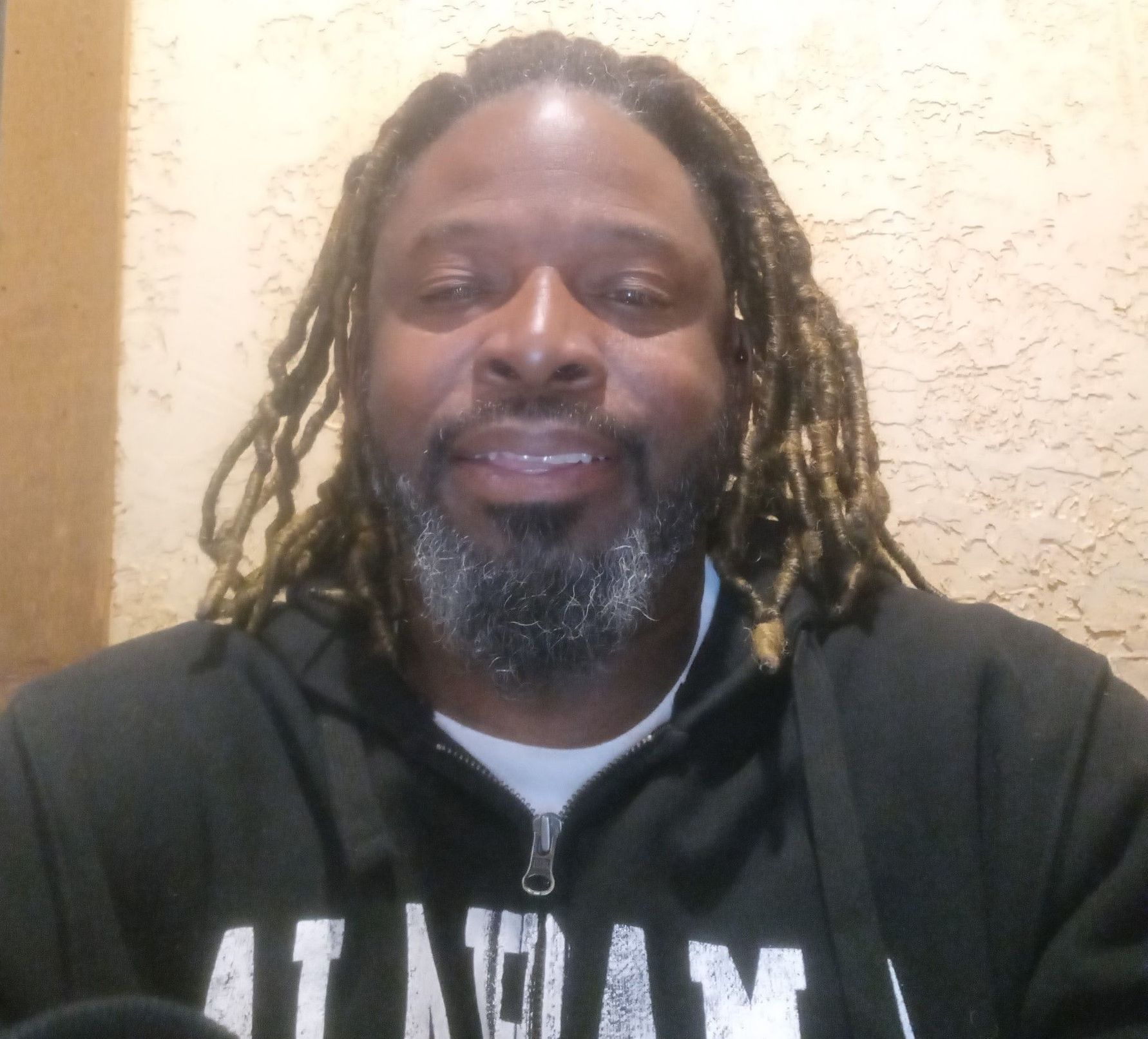 Person smiling in a black hoodie against a beige textured wall