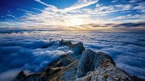Rocky mountain ridge above a sea of clouds at sunrise with blue sky and golden light