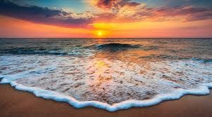 Sunset over the ocean with waves washing onto a sandy beach, pink and orange sky reflected on the water