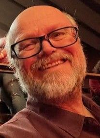 Smiling bald man with glasses and a gray beard in warm indoor lighting