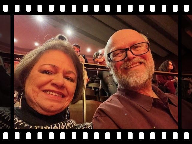 Two smiling people posing in an auditorium, with warm lighting and a filmstrip border.