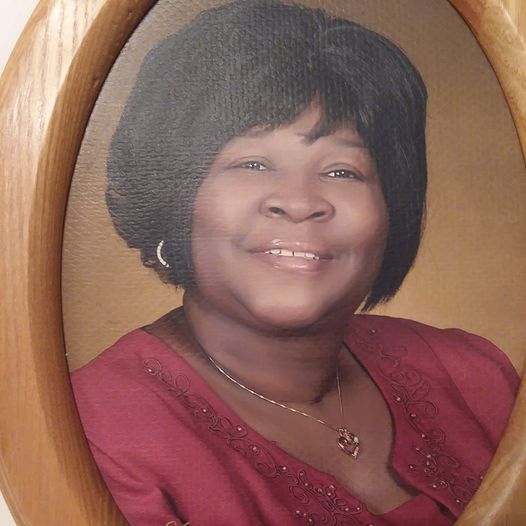 Smiling woman in a burgundy top, posed in a studio portrait with a wooden oval frame.