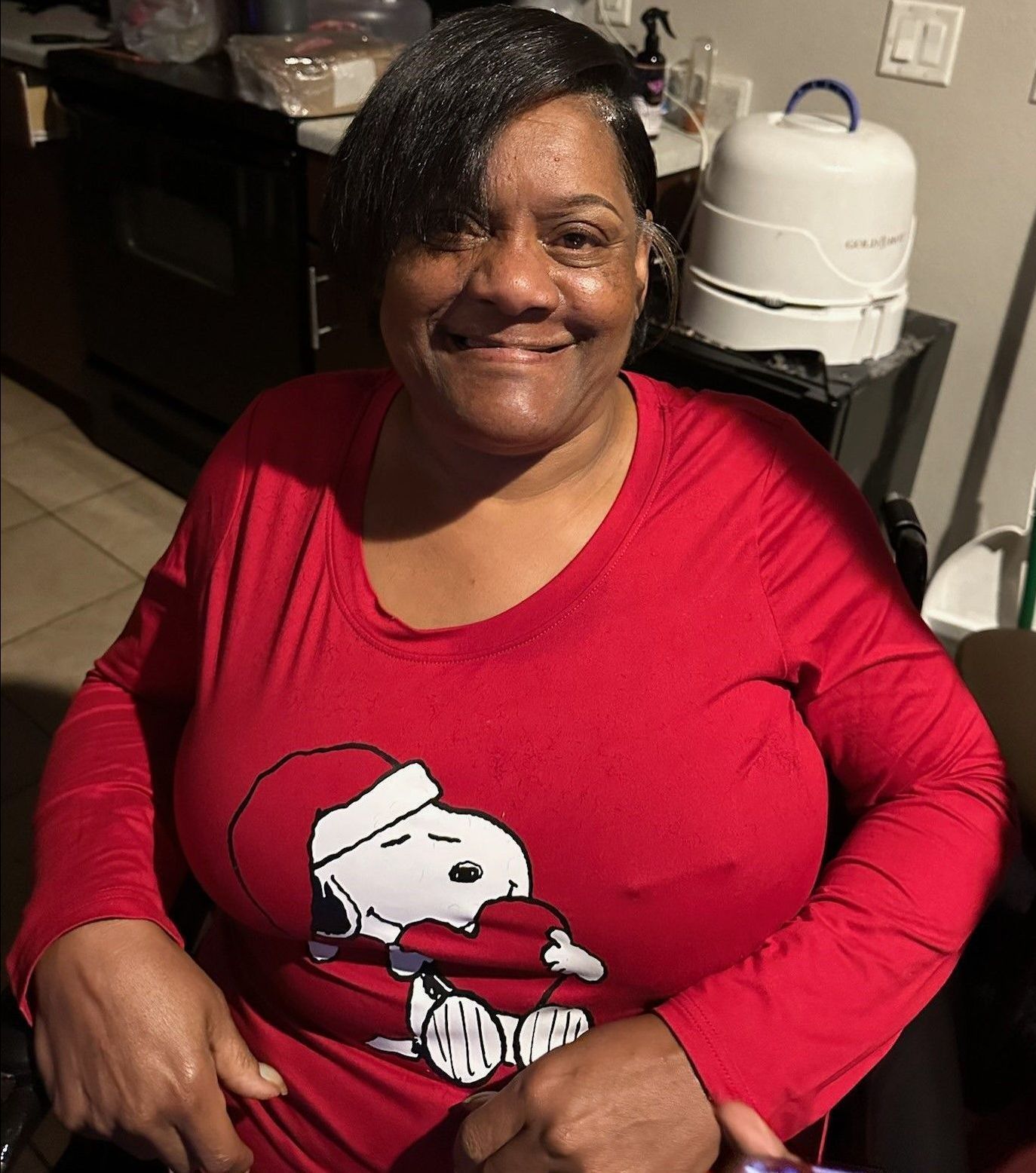 Smiling person in a red Snoopy shirt seated indoors at a table