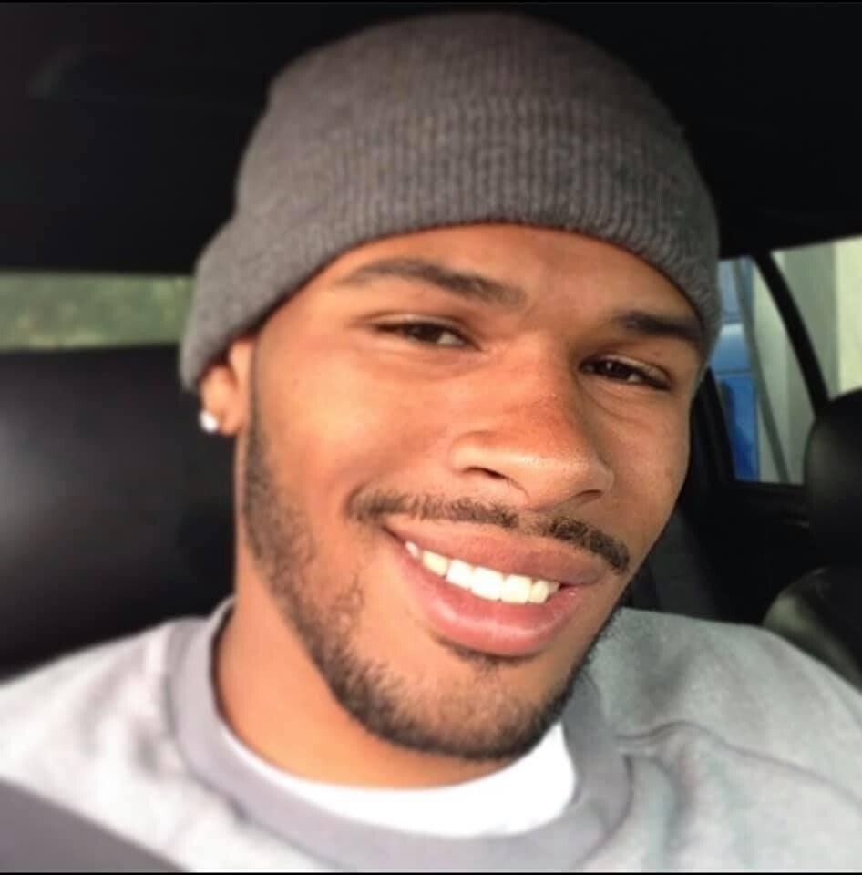 Smiling person in a gray beanie and sweatshirt, taking a selfie in a car