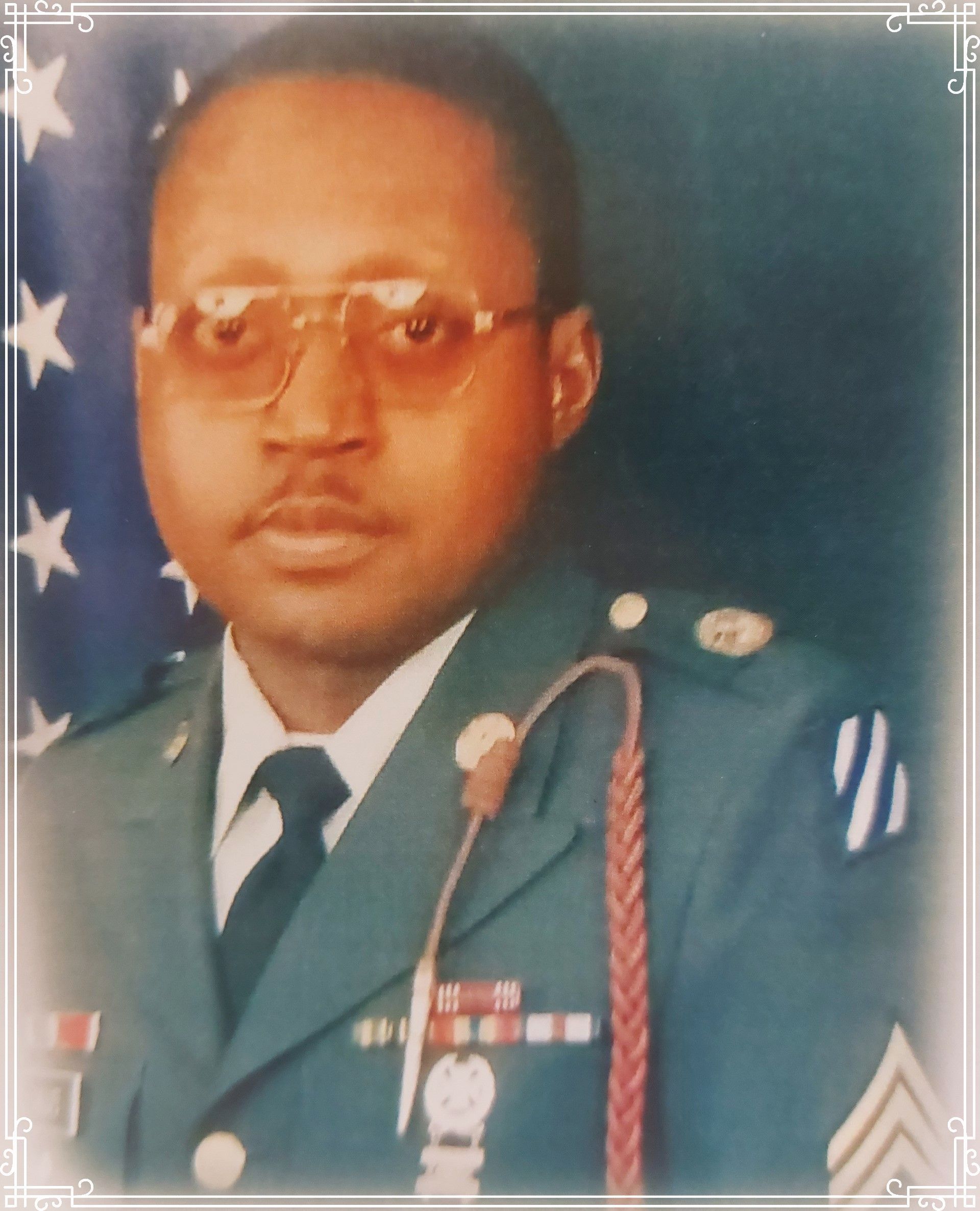 Formal portrait of a person in military uniform with medals, standing before an American flag backdrop