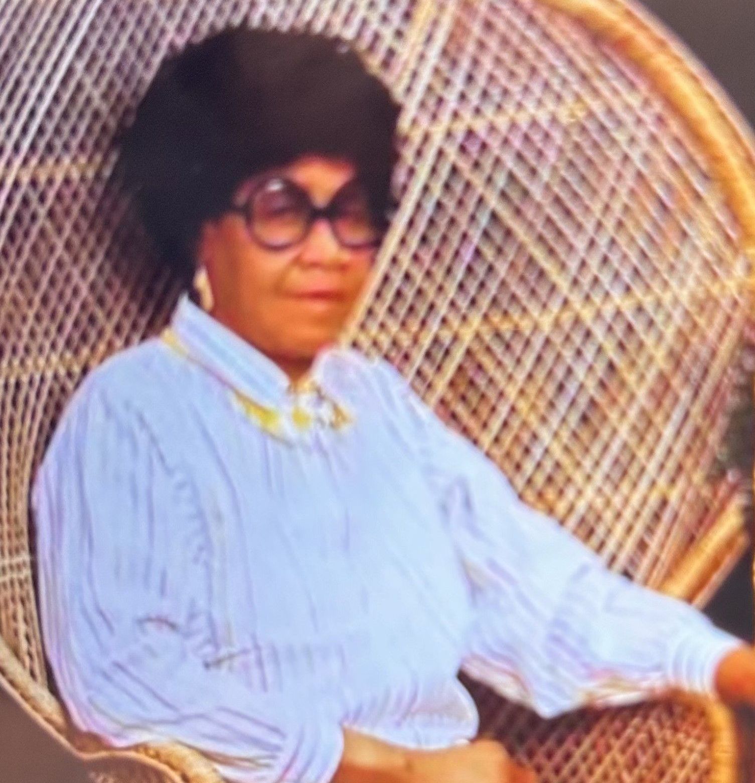 Person in a light blue striped shirt and glasses seated in a wicker chair.