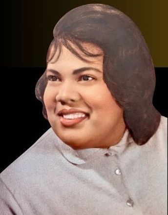 Portrait of a smiling person with dark hair in a light gray top against a dark background