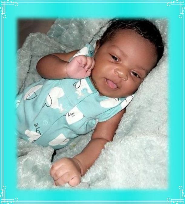 Smiling baby in a turquoise onesie lying on a fluffy white blanket