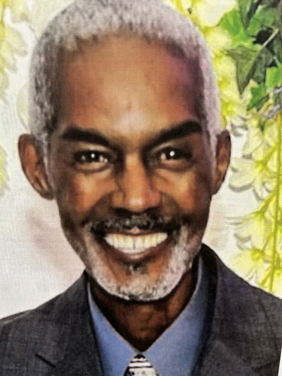 Smiling portrait of a man in a dark suit against a floral background
