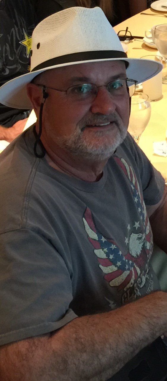 Man wearing a white hat and gray shirt, seated indoors and smiling at the camera.