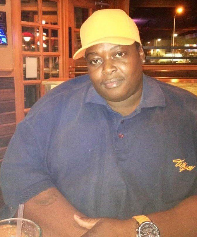 Person in a yellow cap and navy shirt seated at a restaurant table at night.