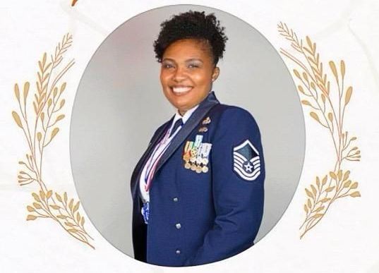 Smiling uniformed service member with medals, posed in a circular portrait framed by gold laurel leaves