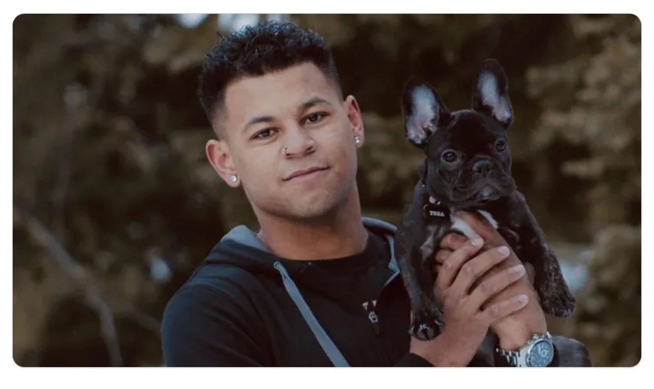 Man holding a small black dog outdoors, both facing the camera.