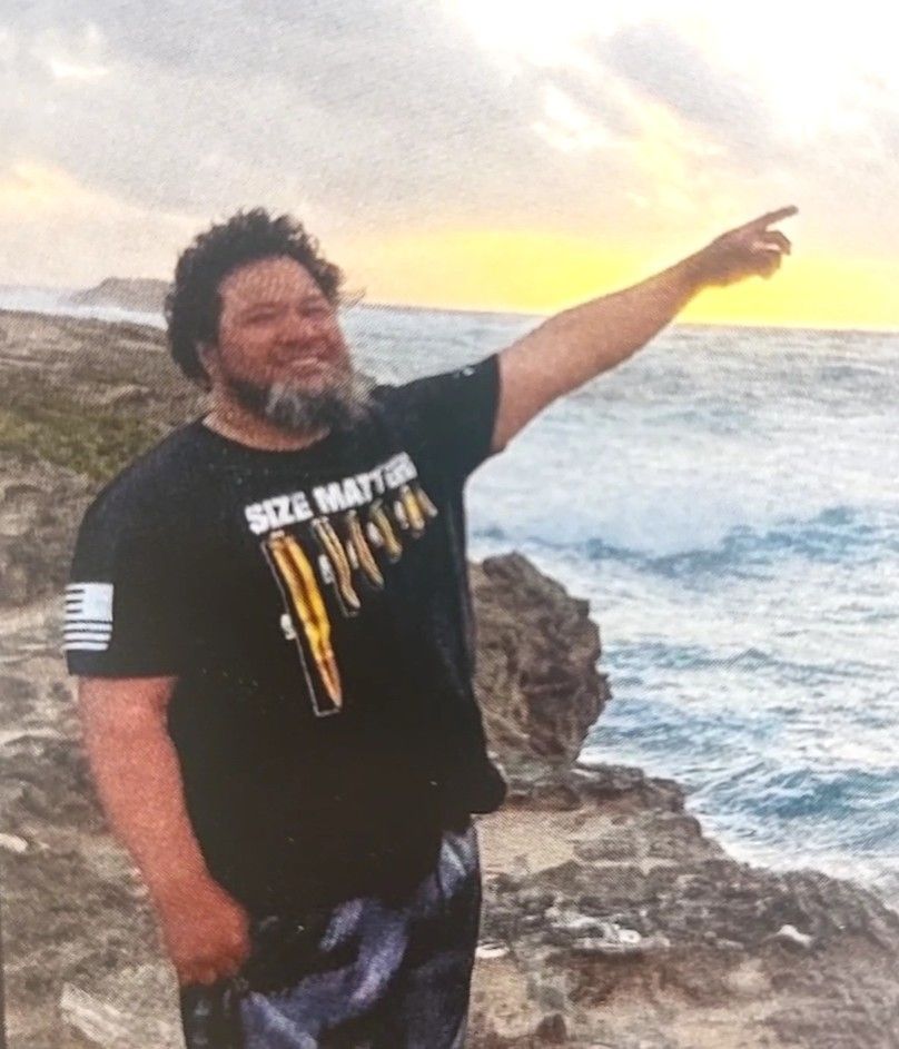Person standing on rocky shore at sunset, pointing toward the ocean while waves crash behind them.