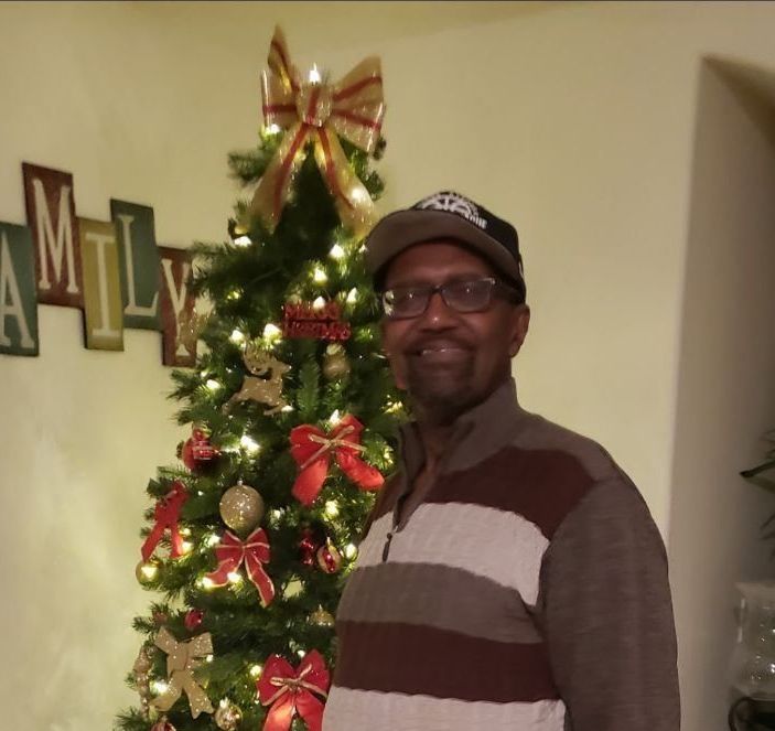 Man smiling beside a decorated Christmas tree with red and gold ornaments