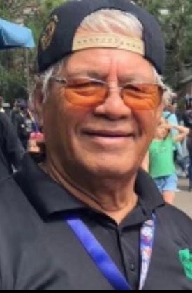 Smiling man in orange-tinted glasses and a backward cap at an outdoor event