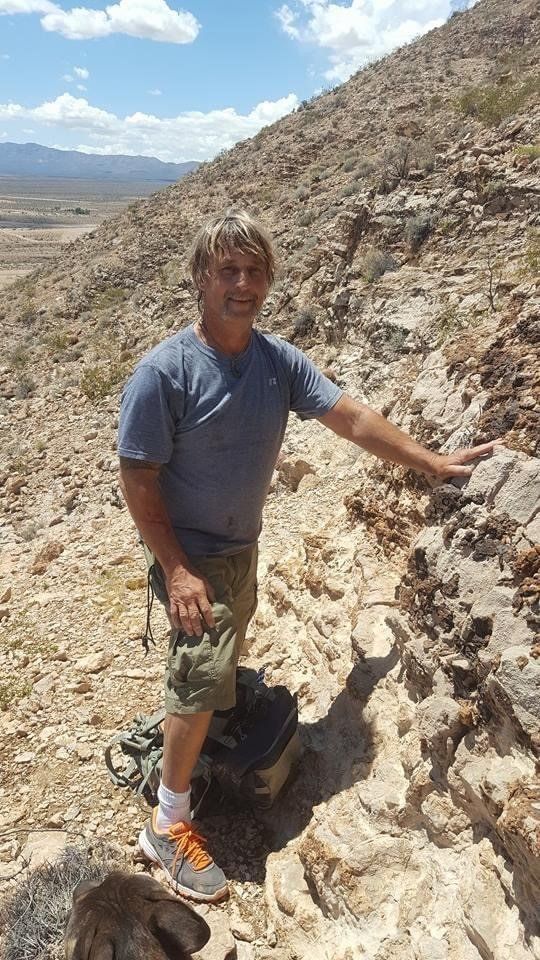 Person standing on a rocky desert hillside, holding a stone and wearing a blue shirt and shorts.