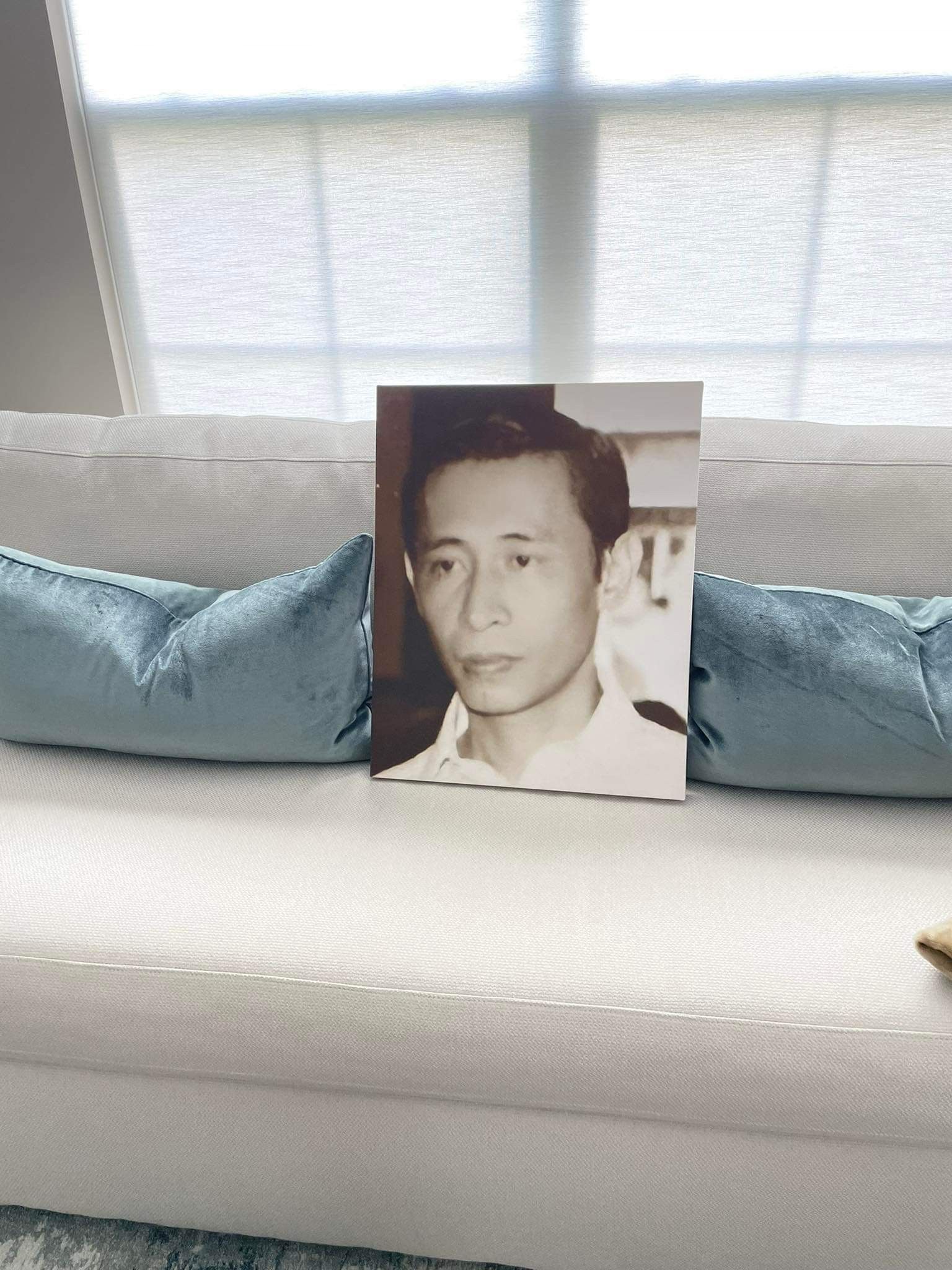 Framed portrait on a white couch with blue pillows in front of a bright window