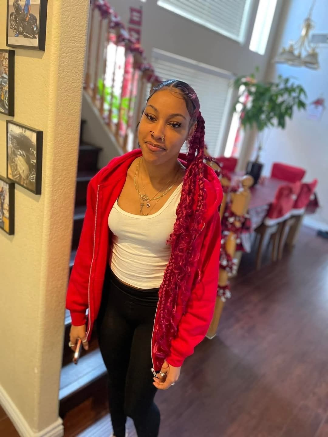 Woman in a red jacket and black pants standing in a hallway at home, holding a phone.