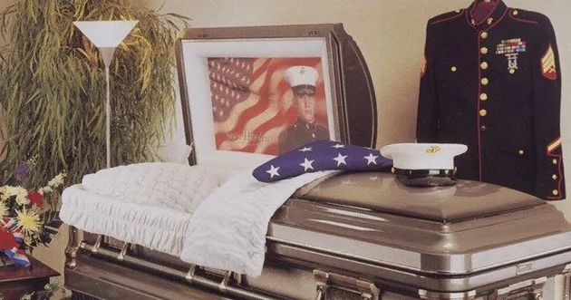 Flag-draped casket with a military uniform and folded American flag at a funeral display