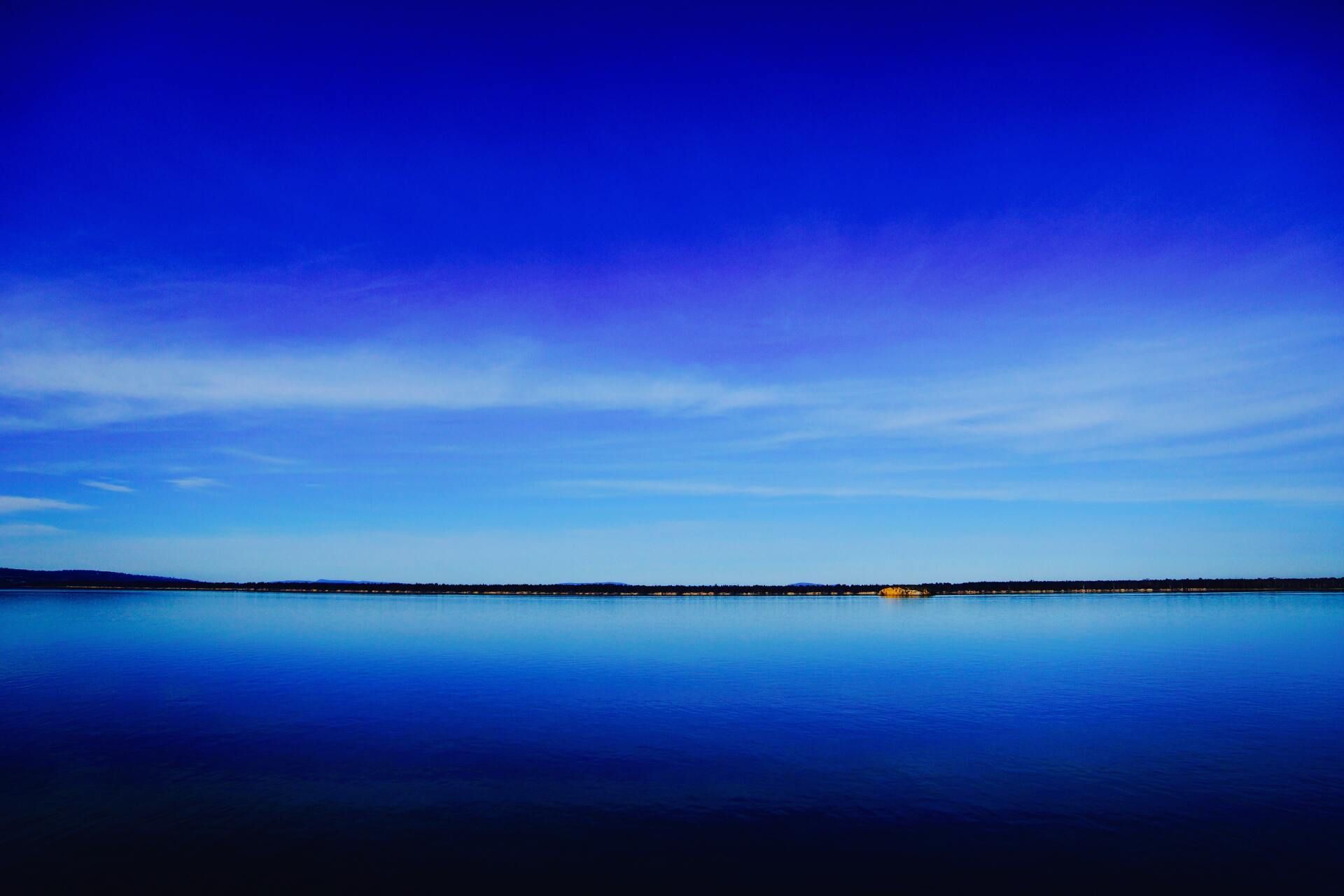 Calm blue lake under a vivid twilight sky, with a distant shoreline on the horizon