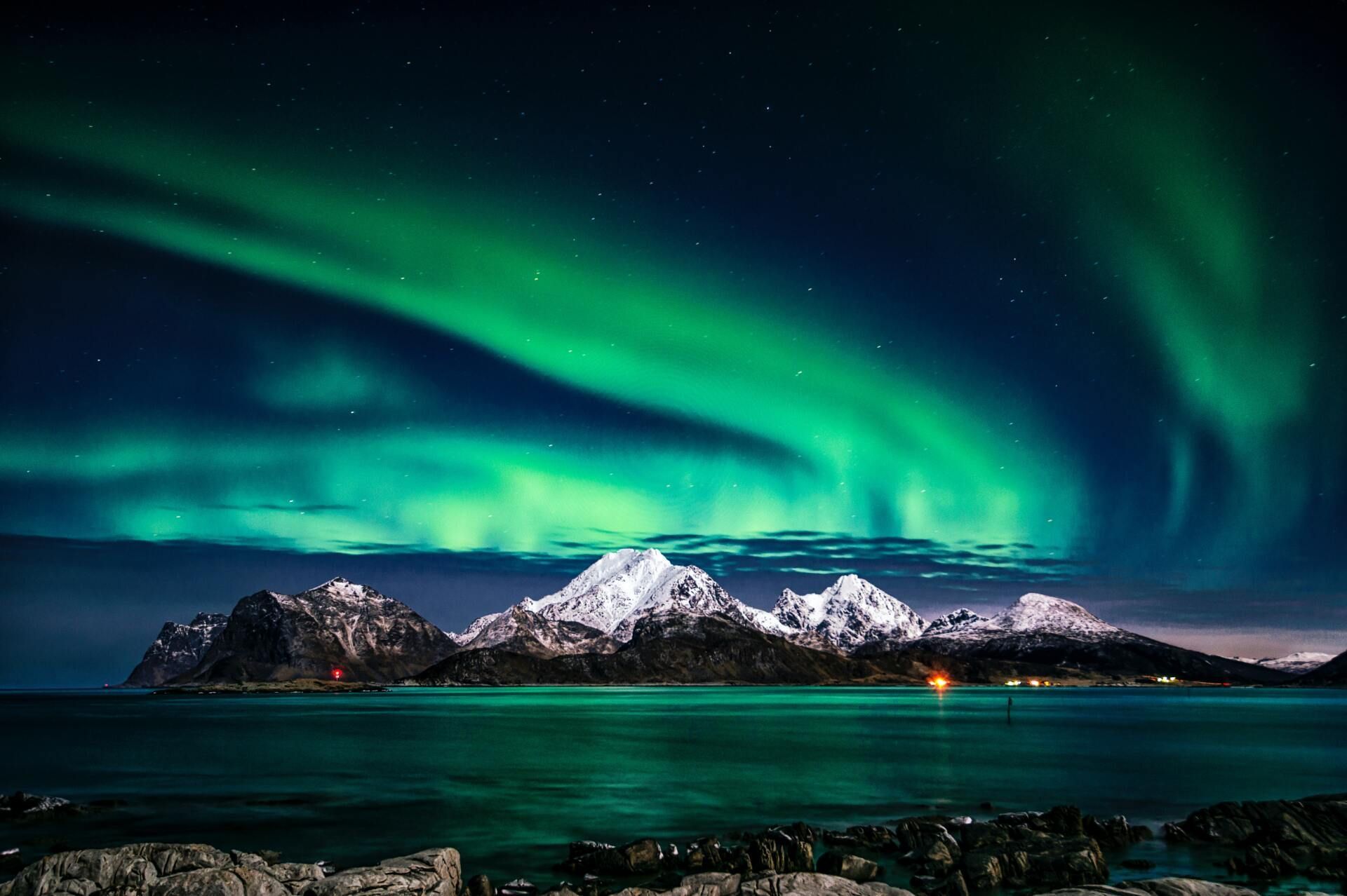 Green aurora over snowy mountains and a dark lake at night