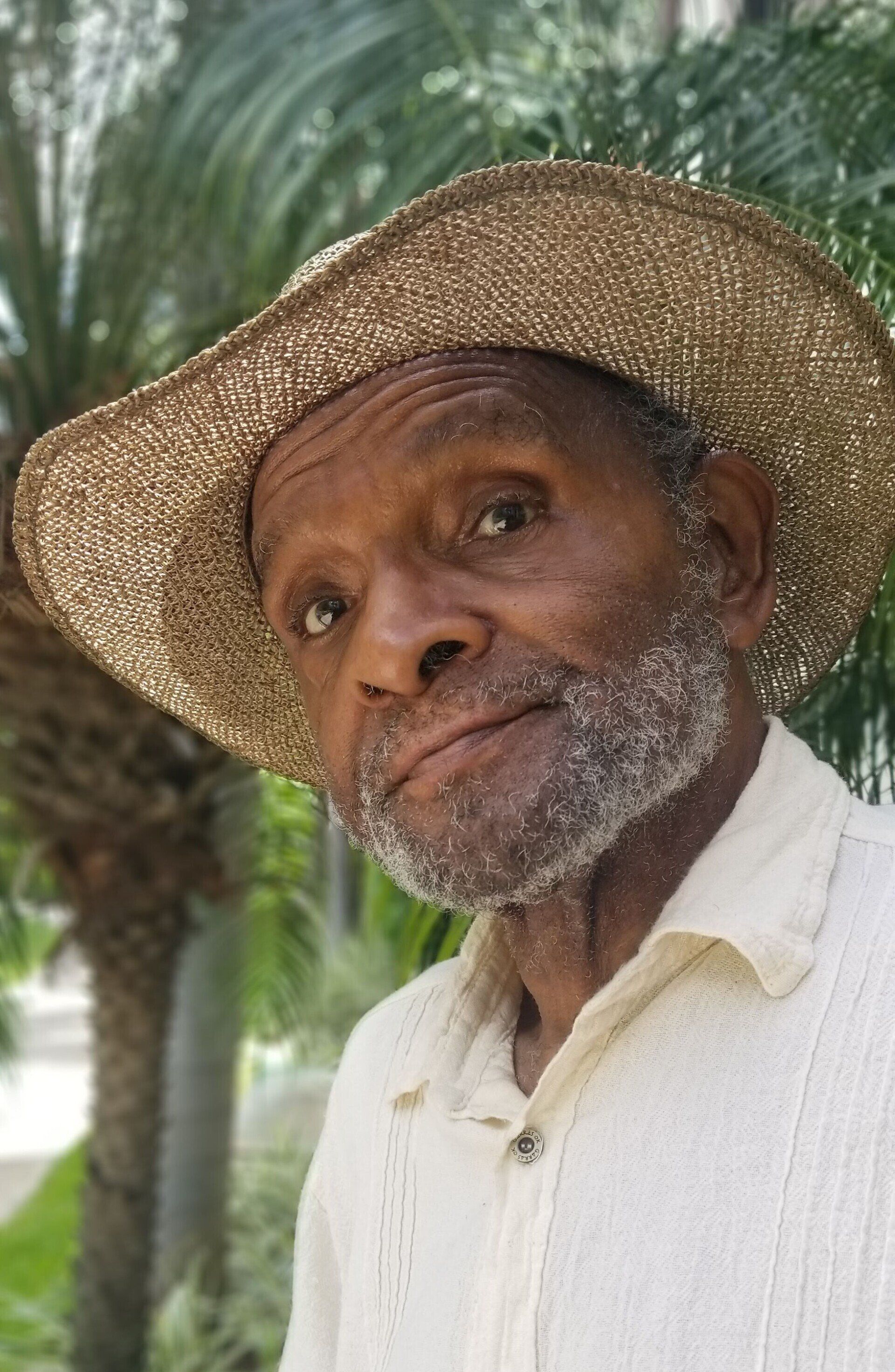 Smiling man in a straw hat and white shirt outdoors, with palm trees in the background