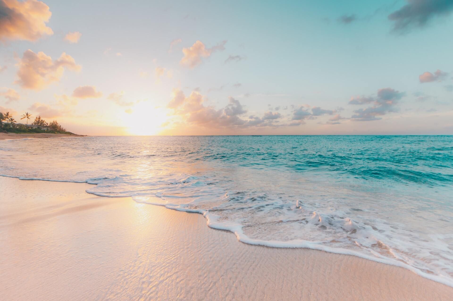 Sunrise over a turquoise ocean with gentle waves on a sandy beach
