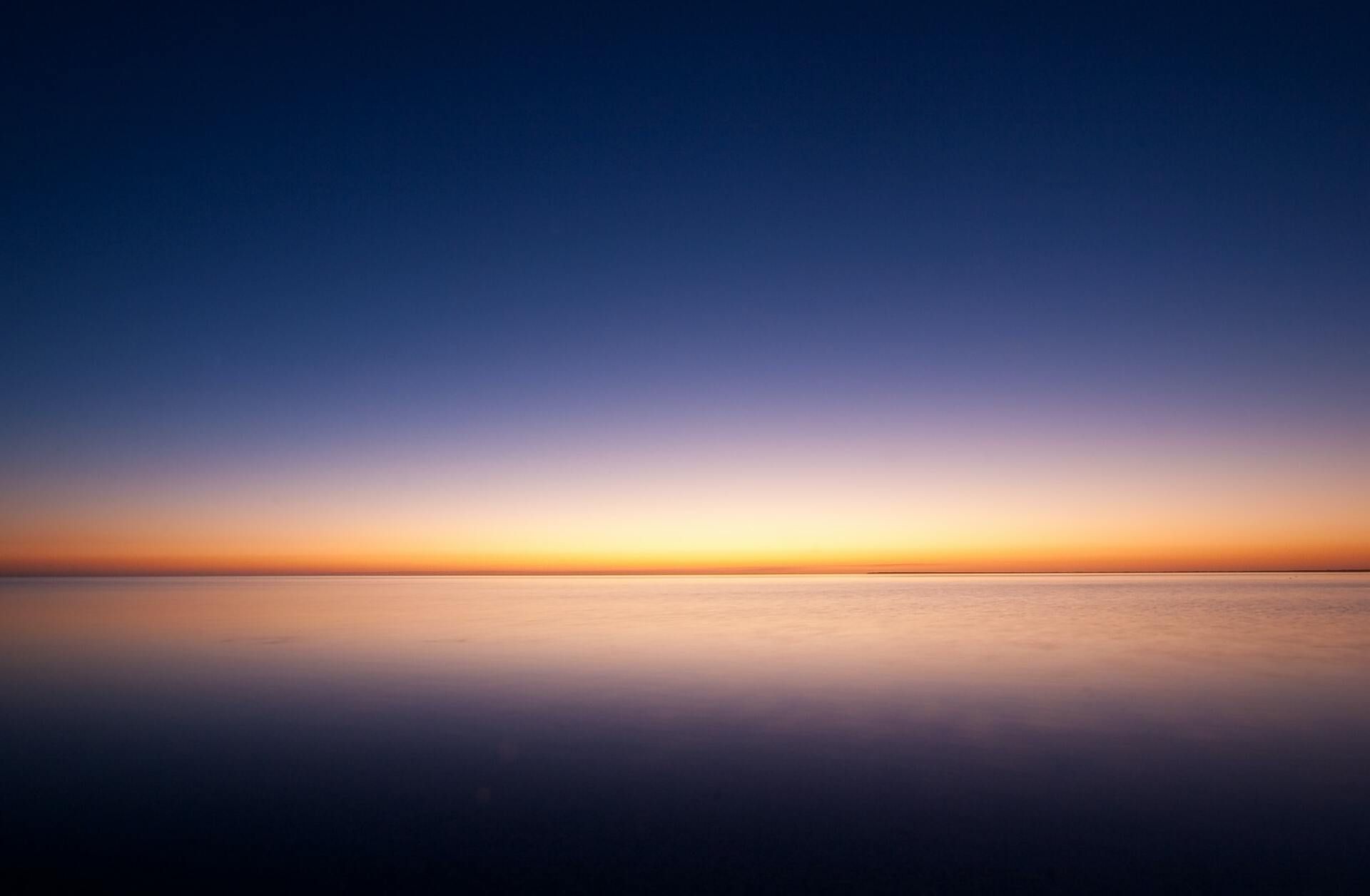 Calm ocean at dawn with a glowing orange horizon beneath a deep blue sky