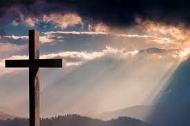 Silhouette of a cross on a hill at sunrise with rays breaking through clouds and mountains in the distance