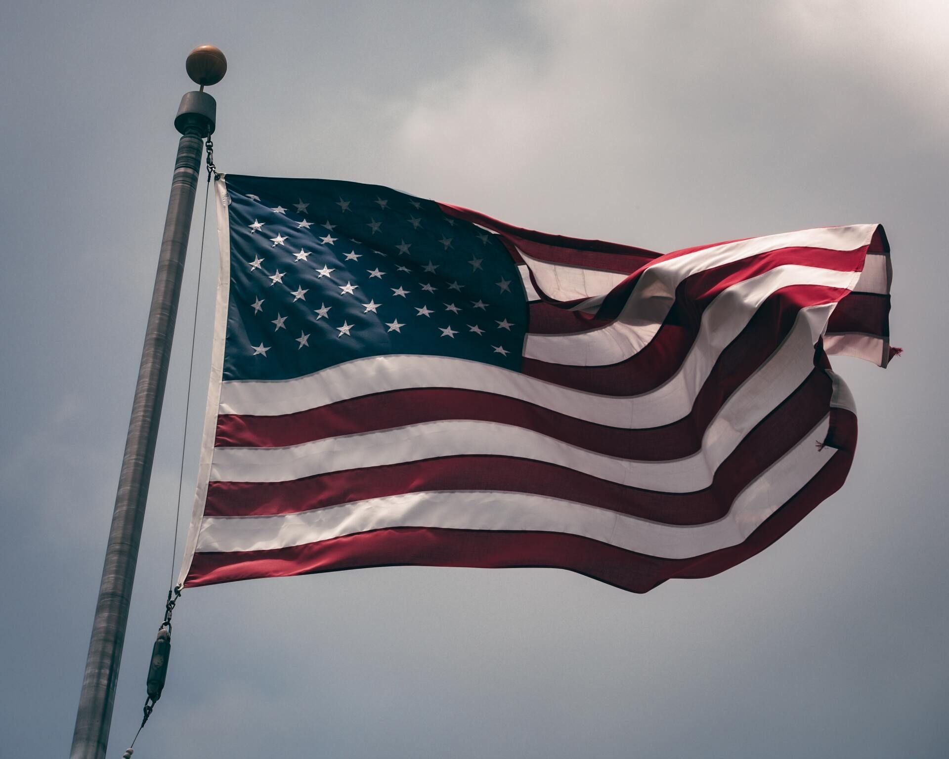 American flag waving on a pole against a cloudy sky.