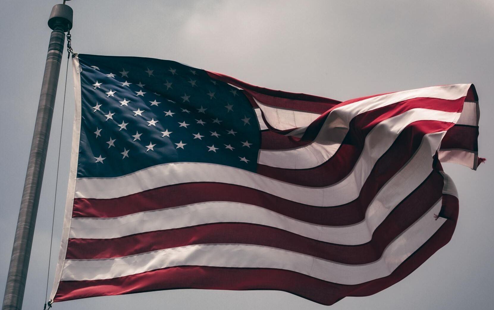 American flag waving on a flagpole against a gray sky