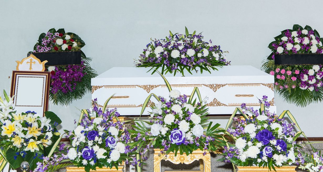 Floral funeral arrangement with white and purple flowers around a casket