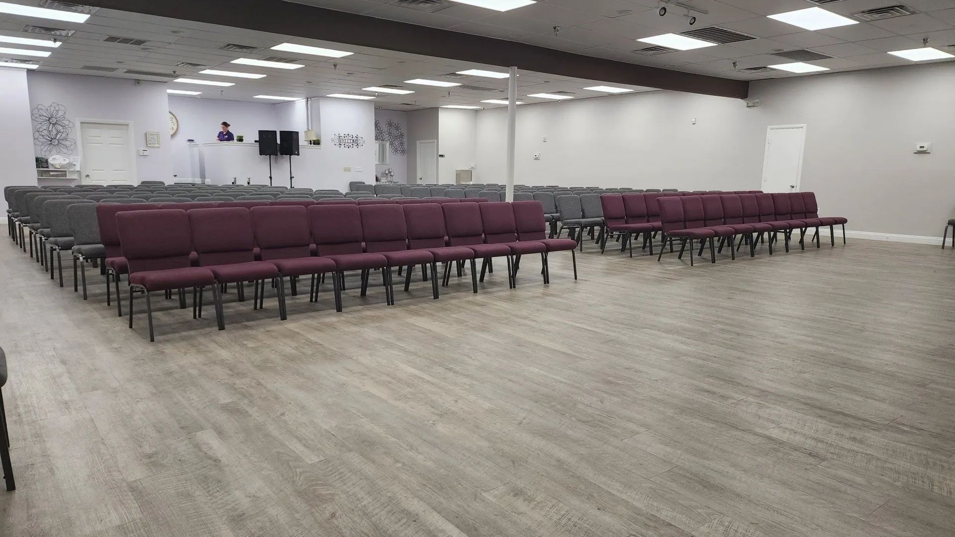 Empty conference room with rows of maroon chairs, white walls, and a wood-look floor