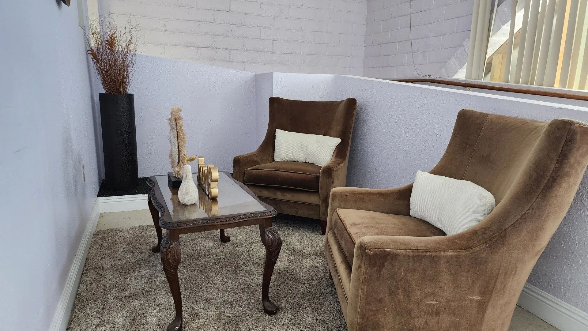 Cozy patio seating with two brown chairs, a small table, and decorative vase on a gravel floor