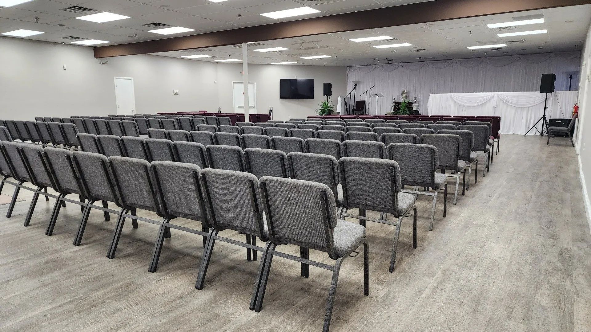 Empty conference room with rows of gray chairs facing a stage area and projector screens