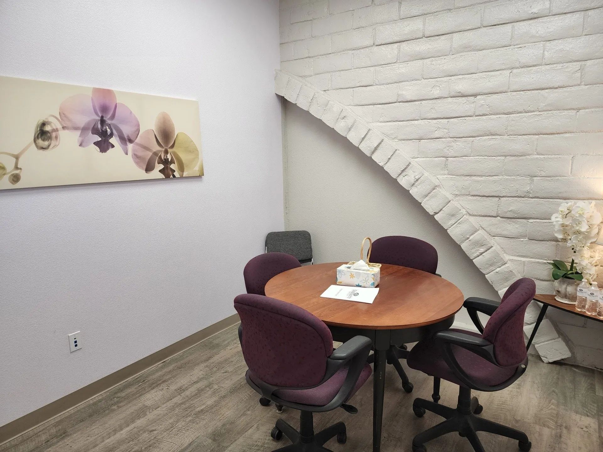 Small meeting room with a round wooden table, four mauve chairs, and a white brick vaulted wall.