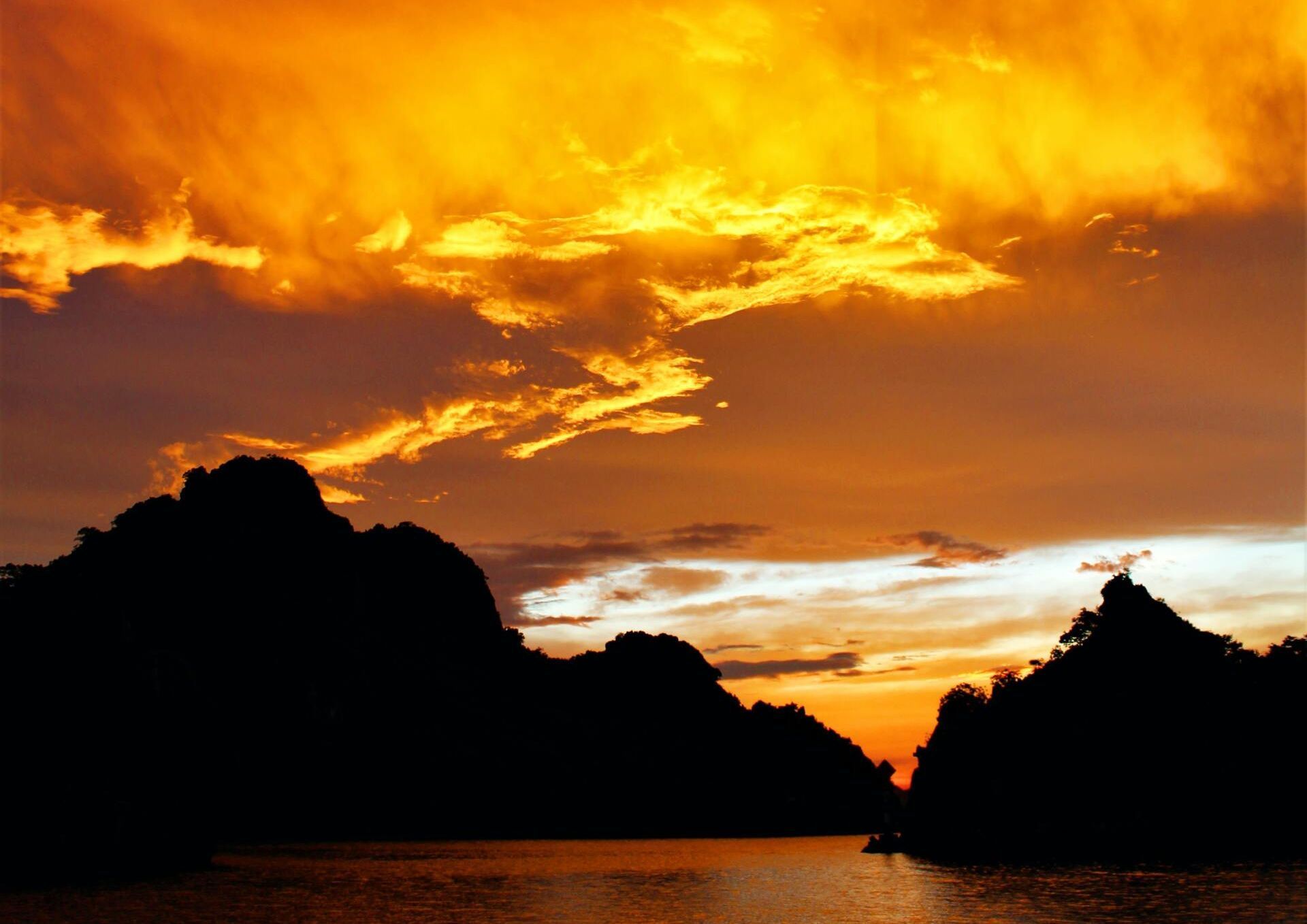 Fiery orange sunset over dark mountain silhouettes and calm water