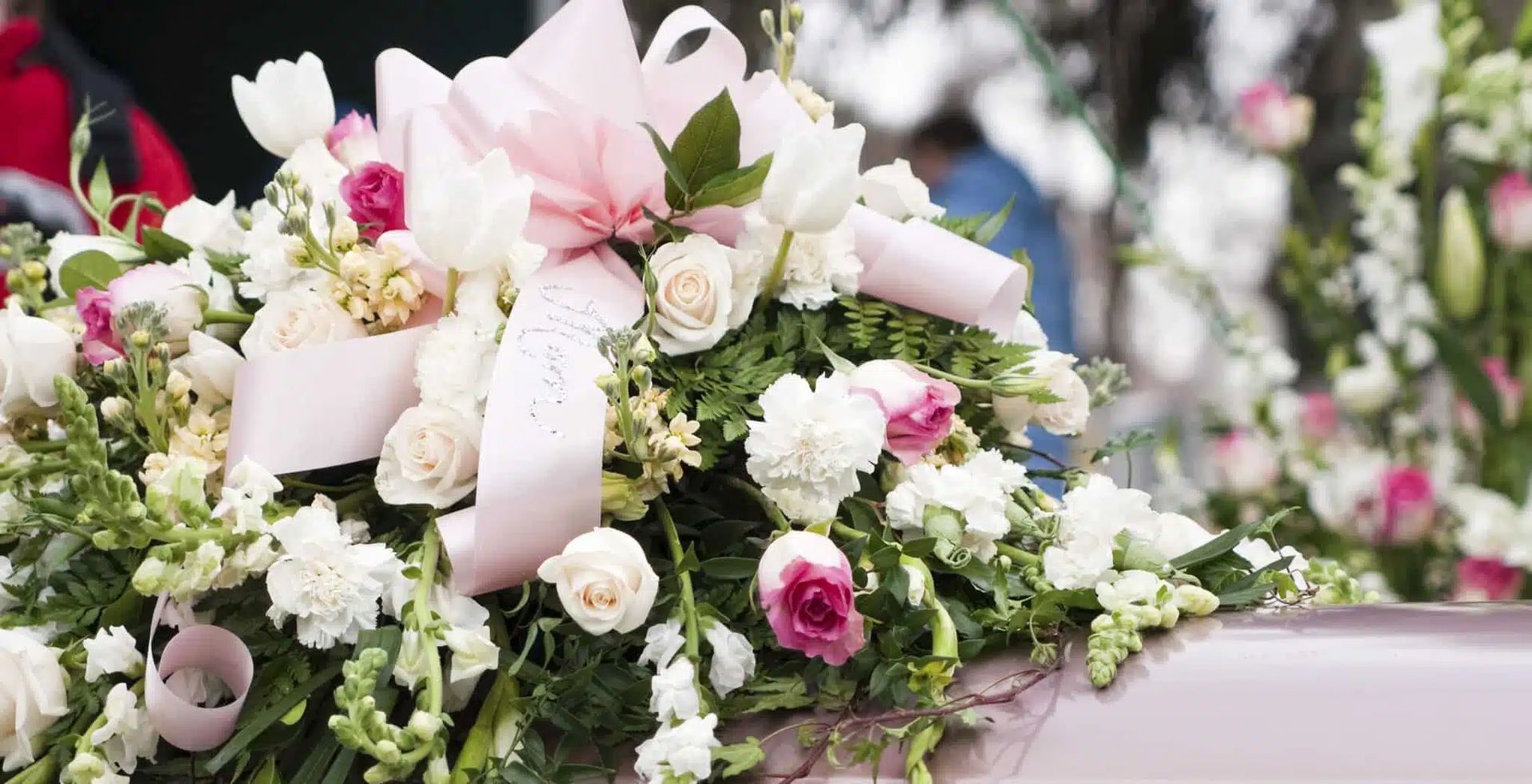 Pink and white funeral flowers on a casket with a satin ribbon bow