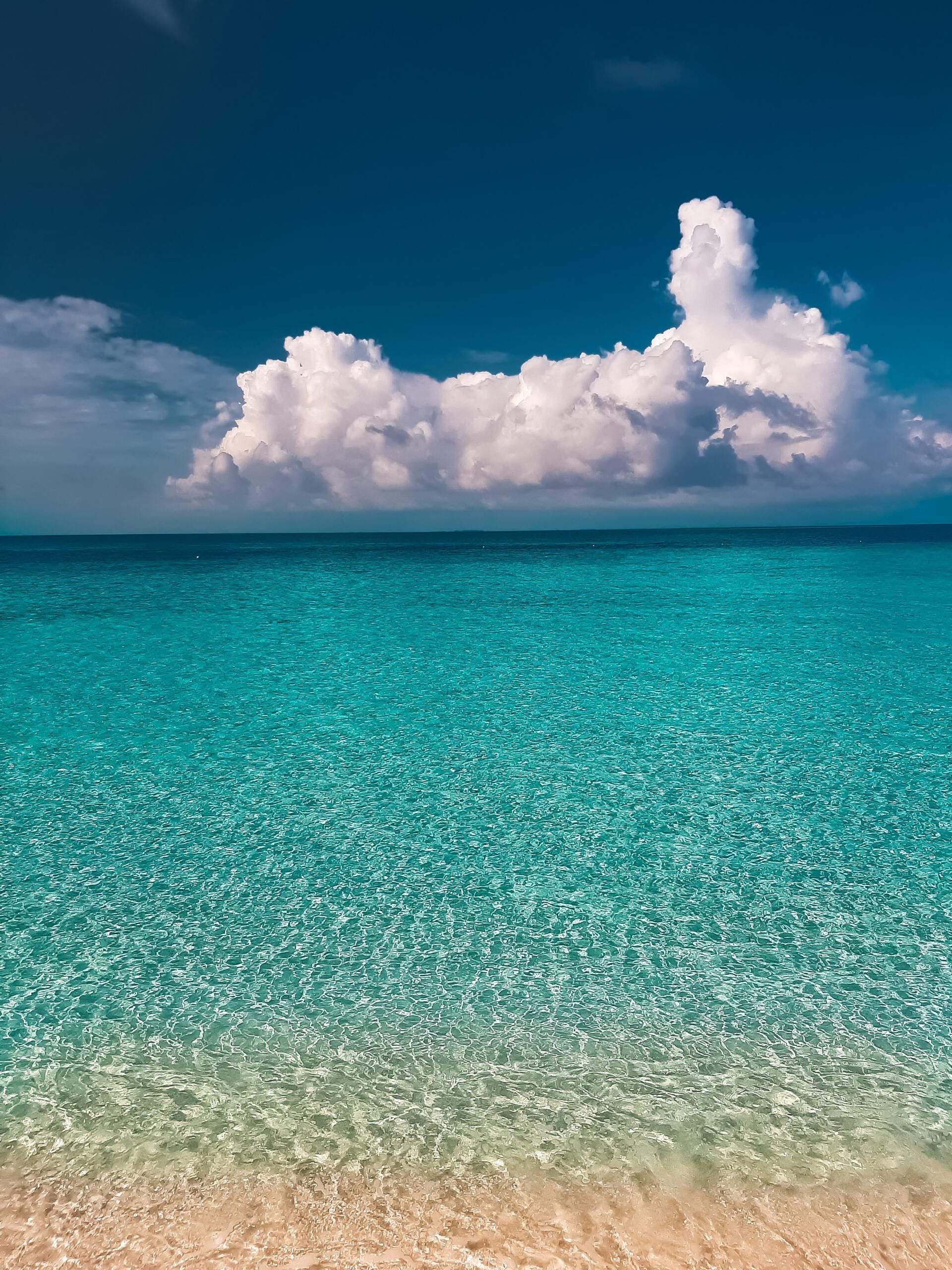 Turquoise ocean under a blue sky with large white clouds, seen from a sandy shore