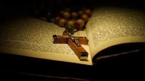 Rosary and wooden cross resting on an open Bible in warm, dim light
