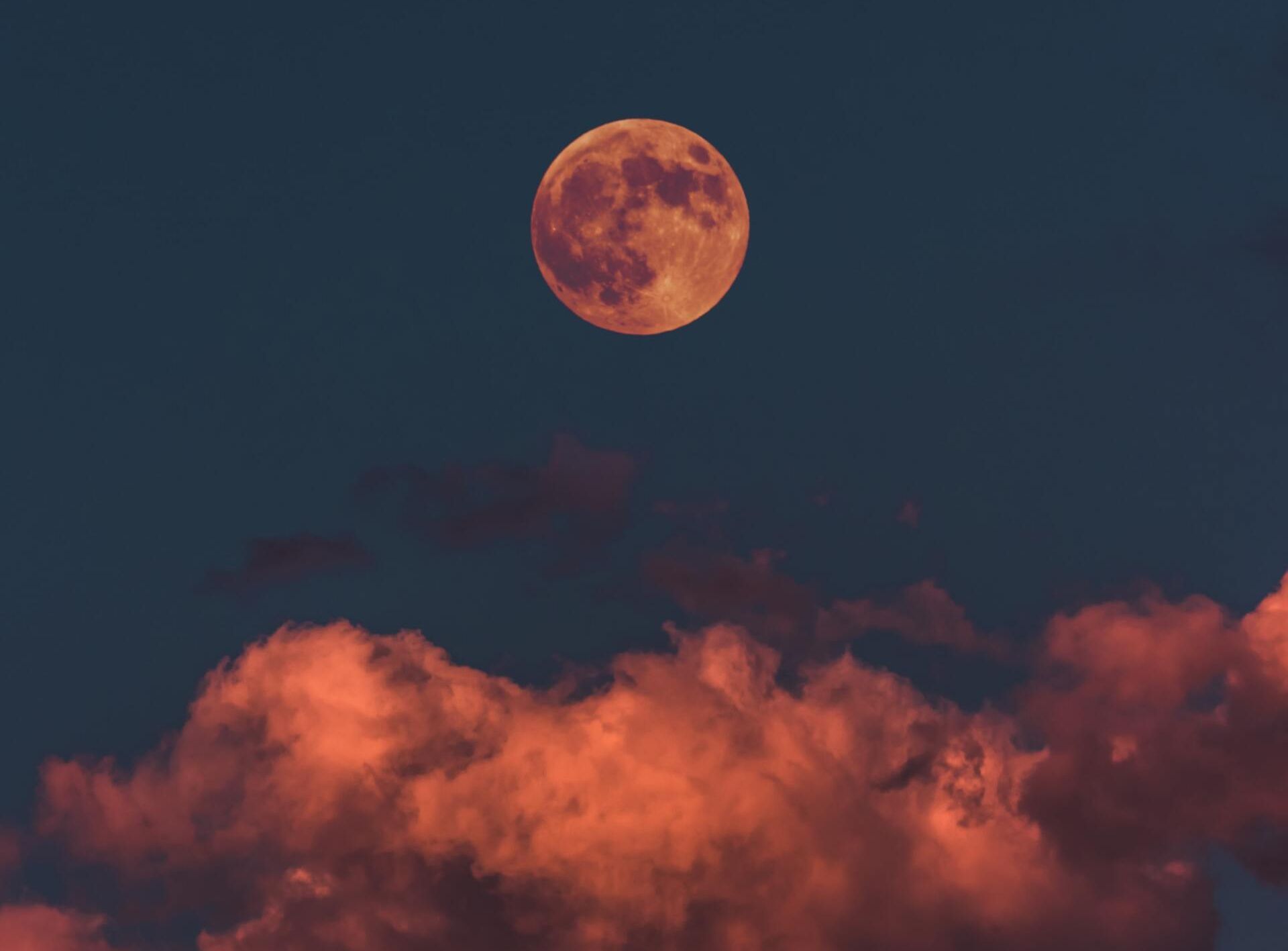Orange full moon above pink clouds in a dark twilight sky