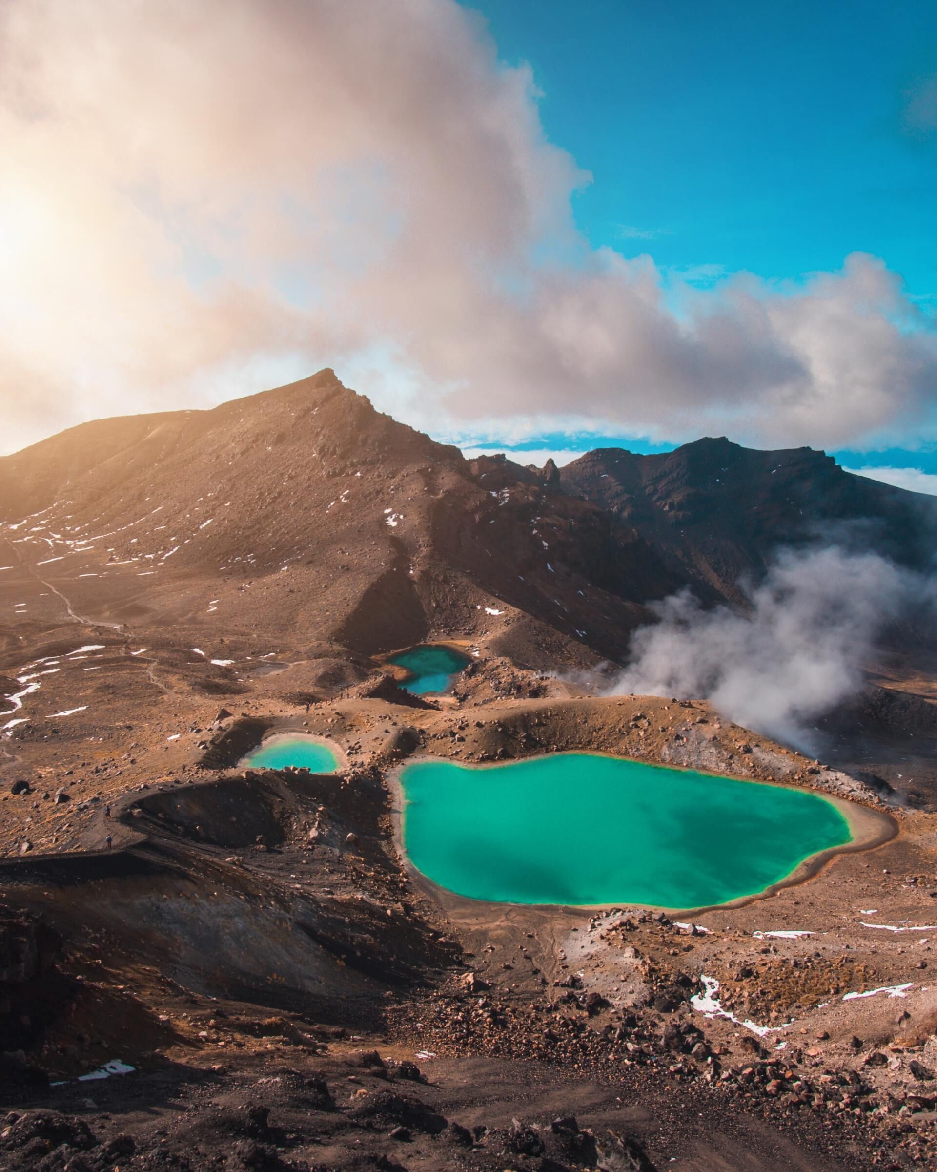 Turquoise alpine lake beside rocky mountain slopes under cloudy blue sky