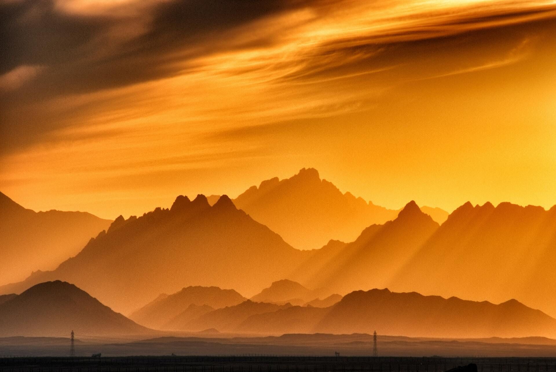 Orange sunset over layered mountain silhouettes with dramatic clouds